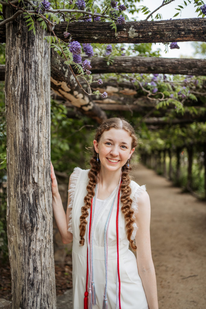 UNC Student posing for graduation photos at Coker Arboretum with purple flowers in bloom