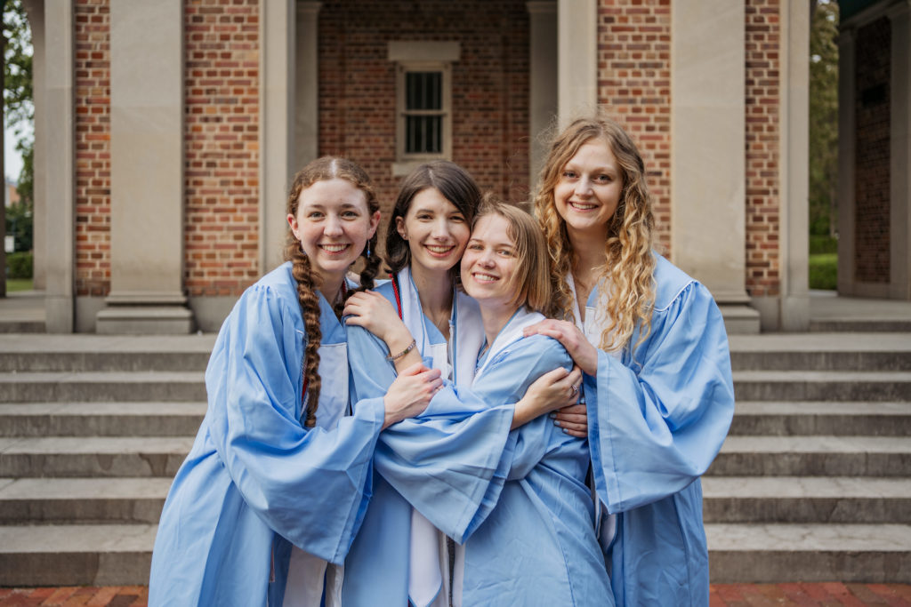 Group of UNC students in cap and gown hugging in front of the Bell Tower