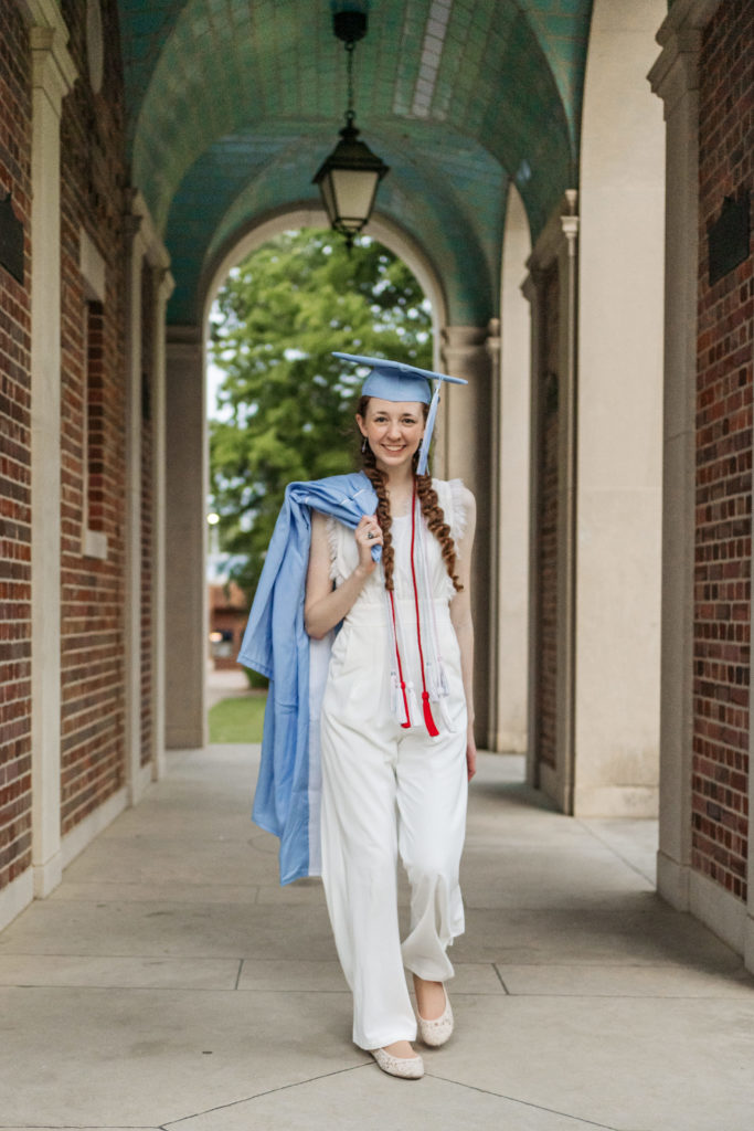 UNC student with cap on holding gown walking under the Bell Tower