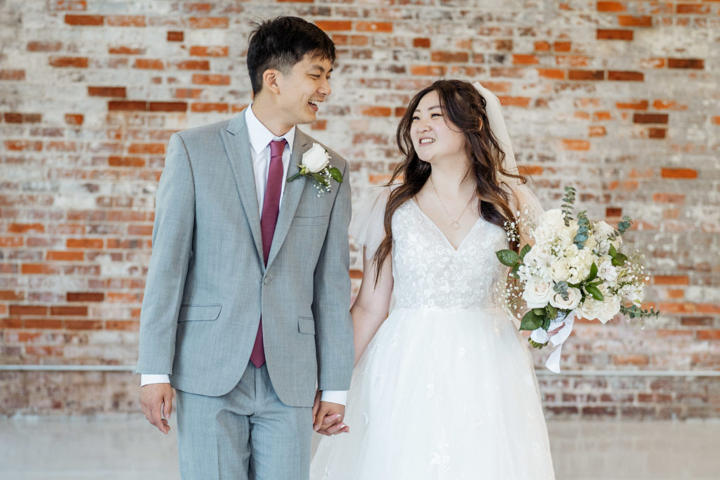bride and groom holding hands and walking in front of brick wall