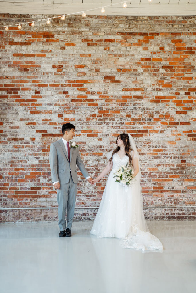 bride and groom holding hands in front of brick wall