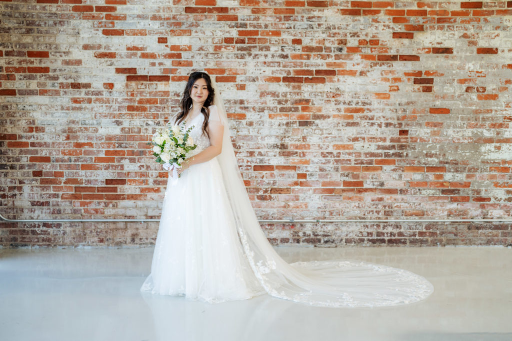 bride standing with bouquet in front of brick wall