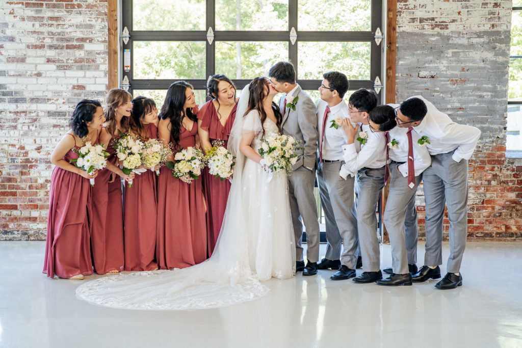 bride and groom kiss while bridesmaids and groomsmen lean in around them