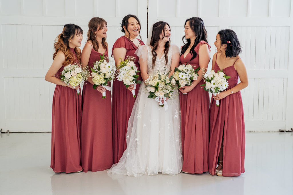 bride laughs with her bridesmaids in front of white barn doors