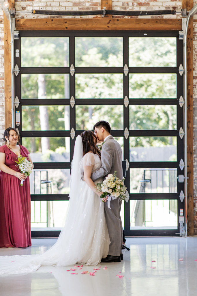 bride and groom kiss in front of large garage door window