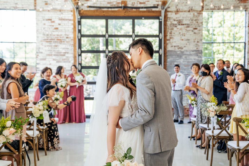 bride and groom kiss down the aisle with guests cheering behind them