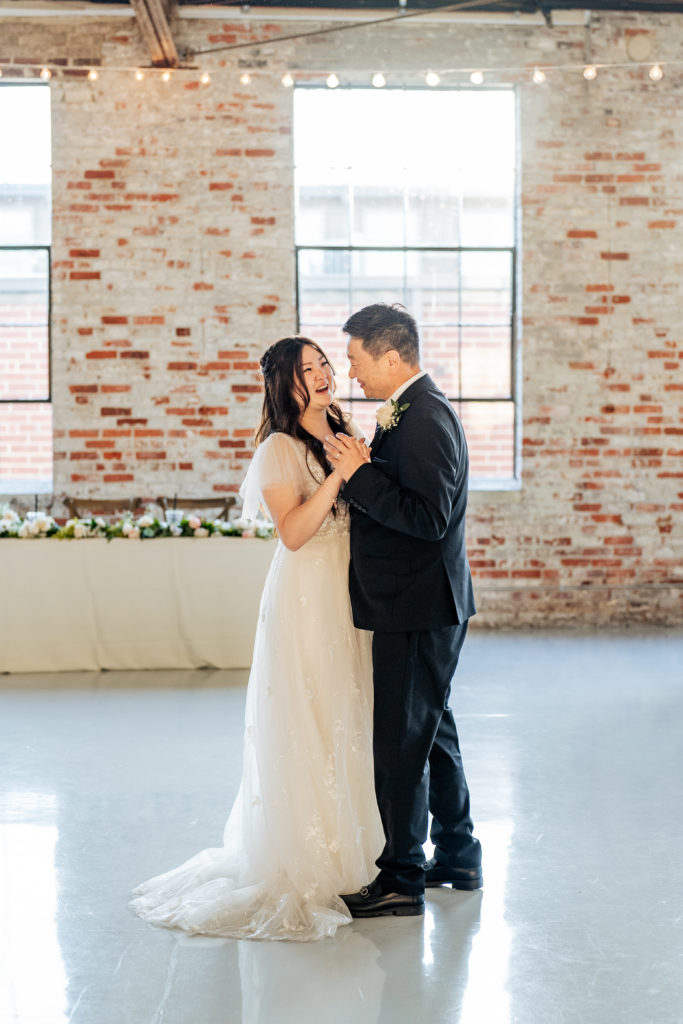 father daughter dance during wedding with brick wall and windows