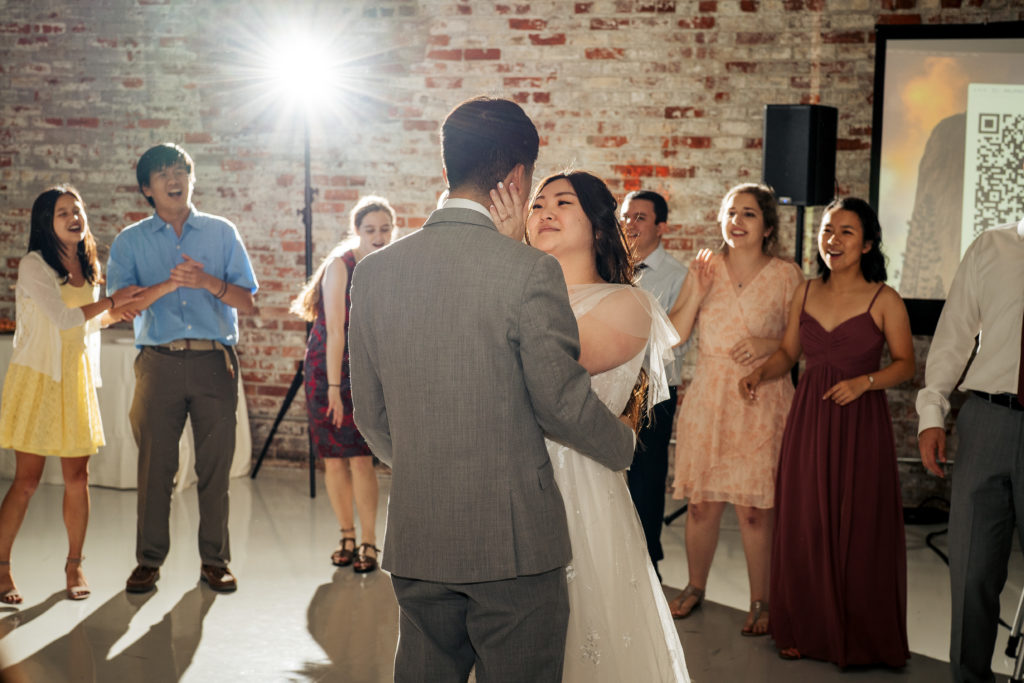 bride holds groom's face on the dance floor with bright flash behind them