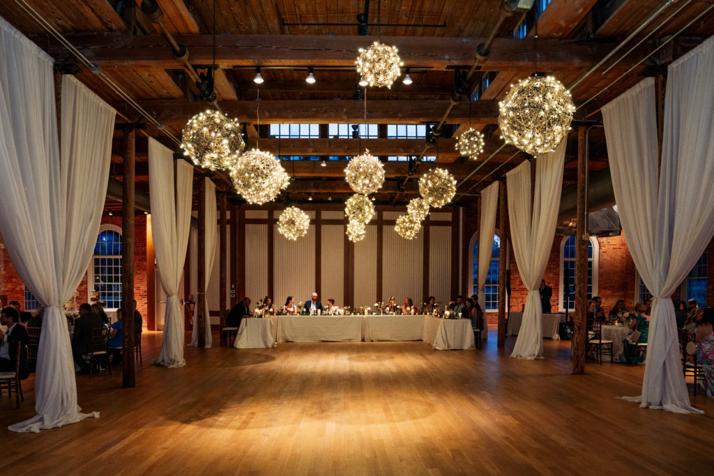 wedding guests dine at head table with decorative balls of light overhead