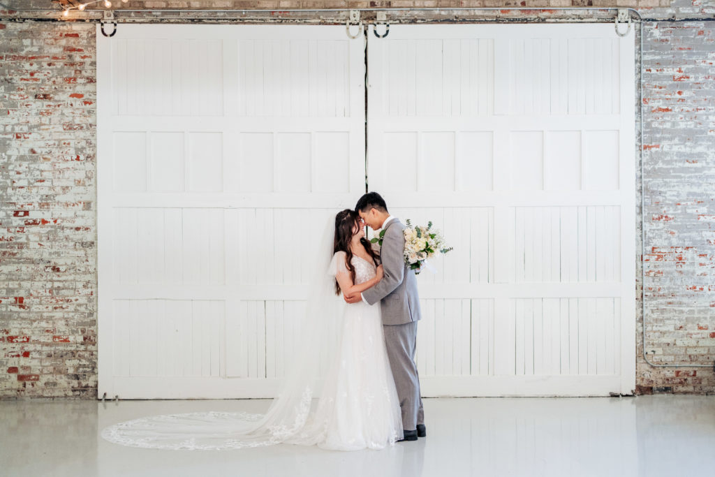 bride and groom embrace in front of white barn doors