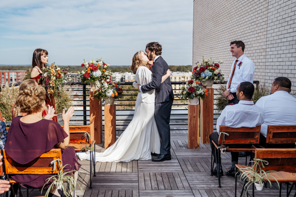 bride and groom kiss during wedding ceremony at the Durham Hotel rooftop