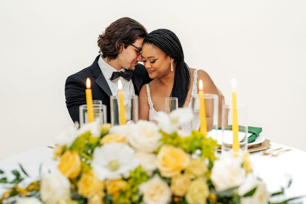 bride and groom snuggle at reception table at wedding in Cary, NC in front of yellow and green flowers