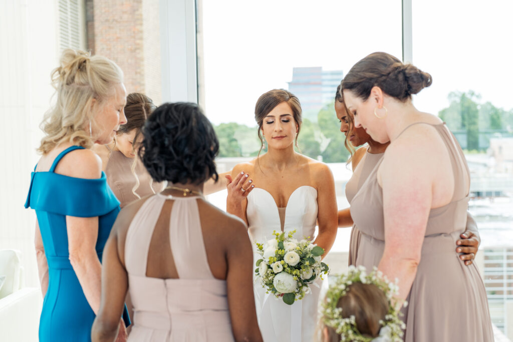 bridesmaids pray over bride before wedding at the Glass Box in Raleigh, NC