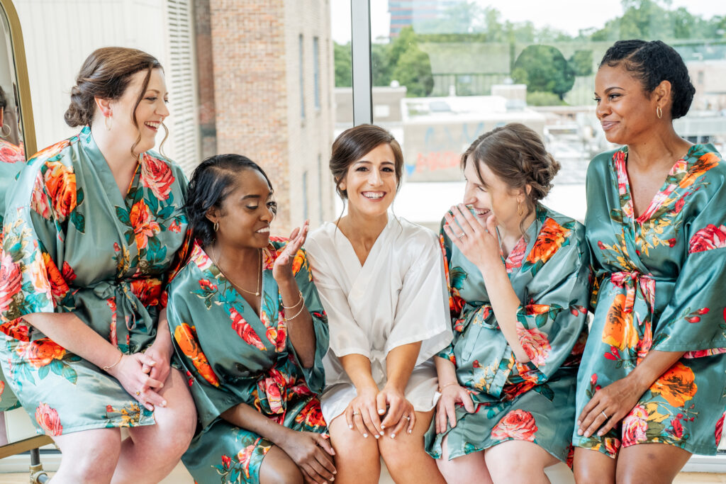 bride smiling with her bridesmaids in robes at the Glass Box in downtown Raleigh, NC