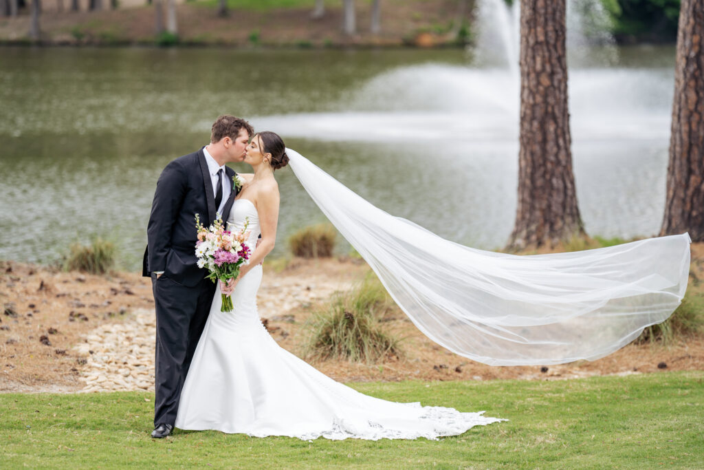 bride and groom kiss in front of lake at MacGregor Downs Country Club