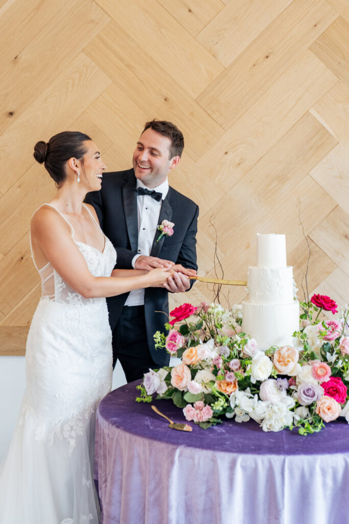 bride and groom cut cake in front of herringbone wall at the Maxwell