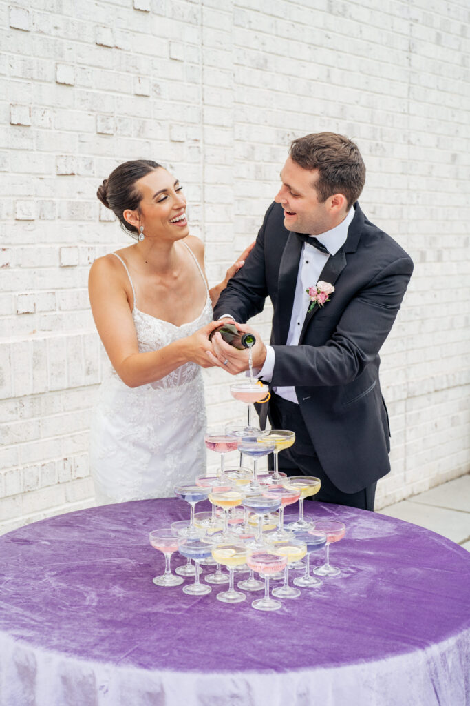 bride and groom pour champagne into colorful cocktail tower