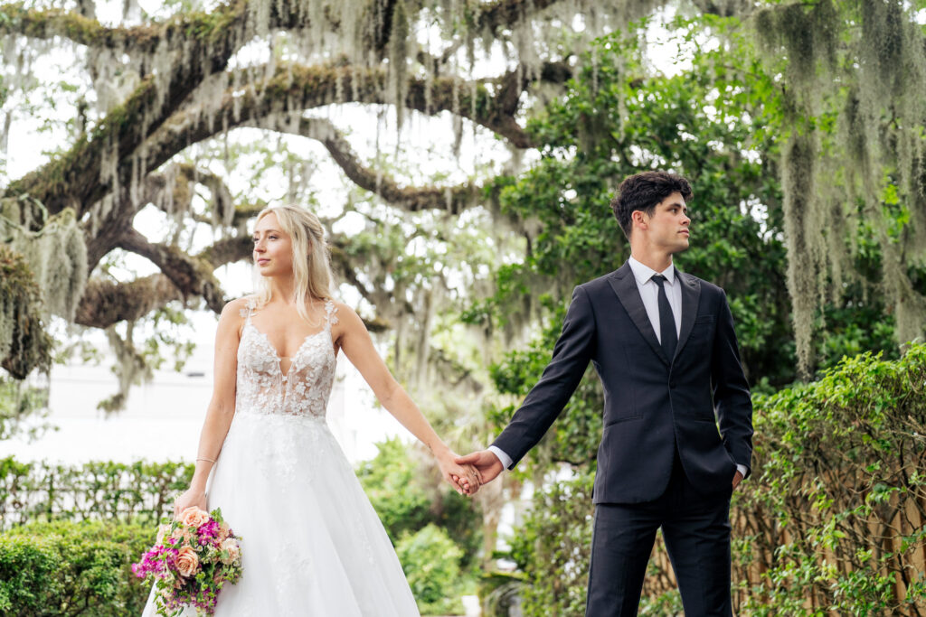 Bride and groom hold hands under Spanish moss covered oak tree in Wilmington, NC