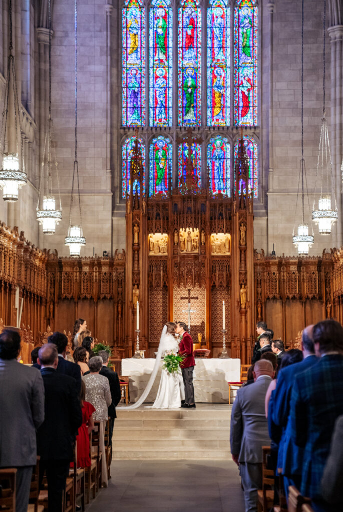 bride and groom kiss in front of stained glass at Duke Chapel wedding