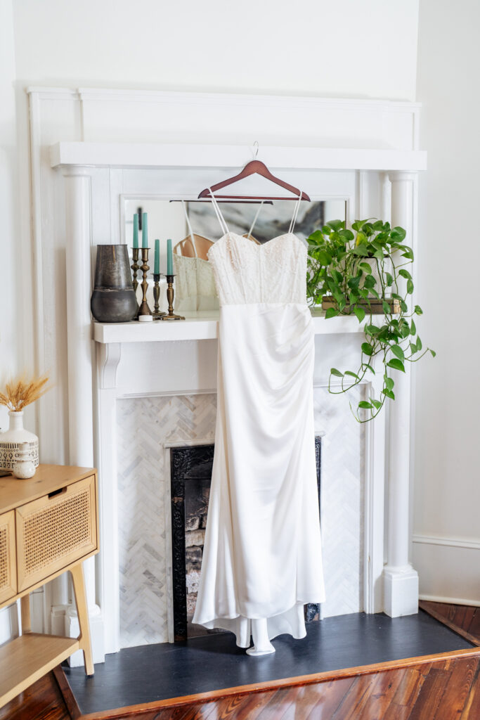 wedding dress hanging in front of a white fireplace mantel