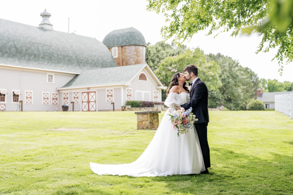 bride and groom kiss under a tree in front of the Historic Wakefield Barn near Raleigh, NC