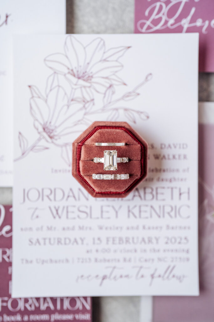 wedding rings in rose colored velvet ring box on top of wedding invitation