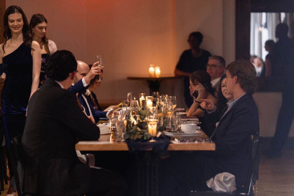 Groomsman raises a glass for a toast during dinner at a wedding at Bridge Club in Raleigh, NC